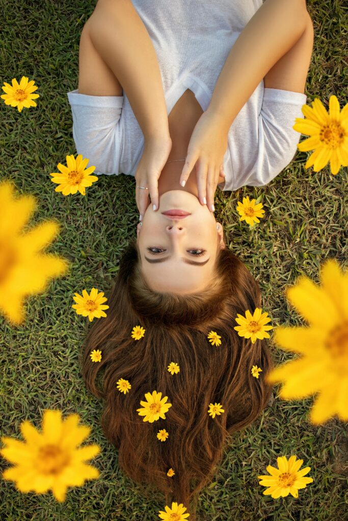 Upside down portrait of a woman lying on grass with yellow flowers in her hair.