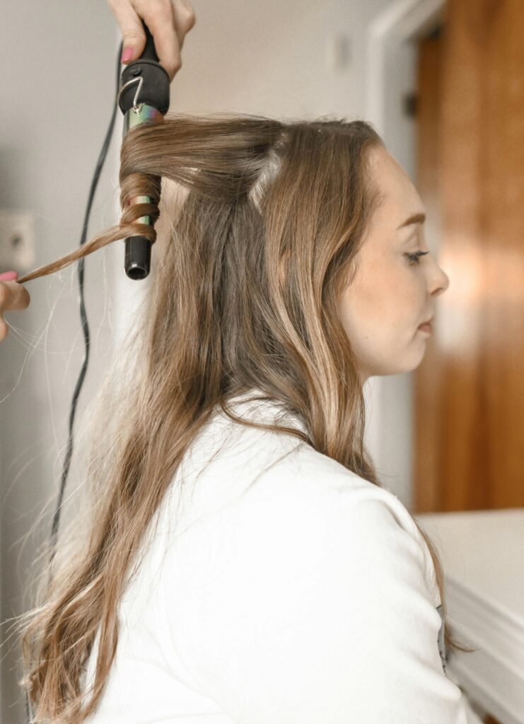 Profile of a woman having her hair curled with an iron in a salon setting.